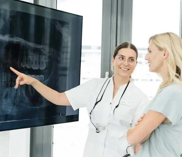 Zahn&auml;rztin erkl&auml;rt einer Patientin ihr R&ouml;ntgenbild am Bildschirm und zeigt auf das Bild